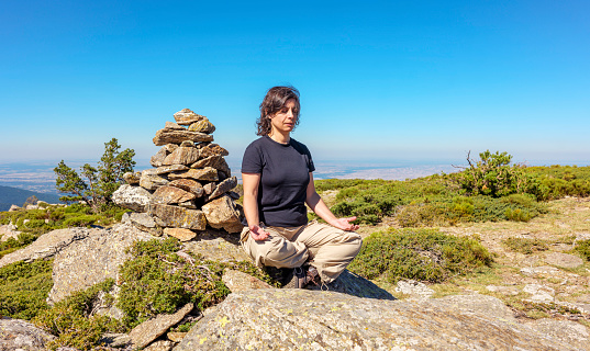 Middle-aged caucasian woman sitting next to a milestone in easy position for a meditation exercise in the midst of nature.