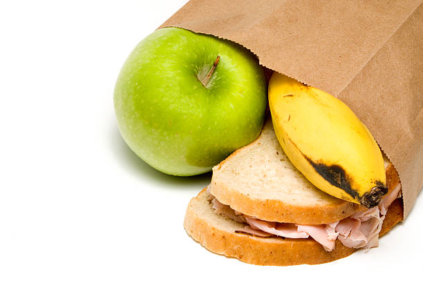 Paper bag with an apple, sandwich, and banana falling out stock photo