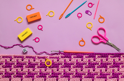 Workplace with bright pink purple crochet fabric and crochet tools on a lilac background. Top view. Copy space.