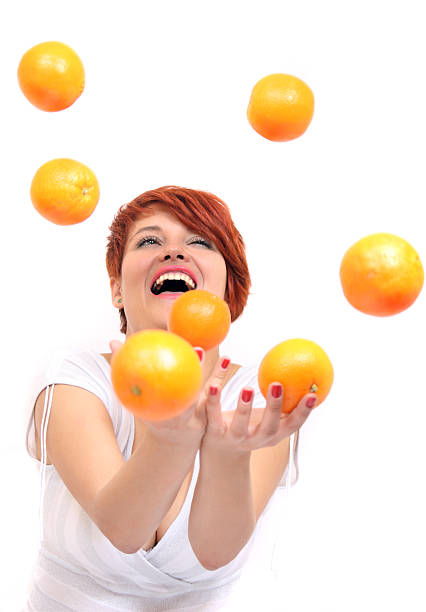 A girl with red hairs smiles and juggles orange on a white background.Similar images