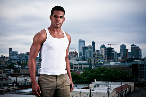 Urban guy, handsome young African American male outside in daylight with urban city background.