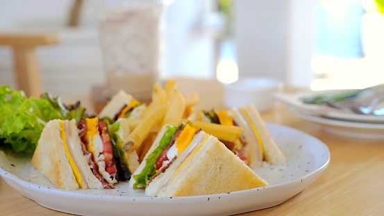 Club sandwich and French fries on white plate in cafe