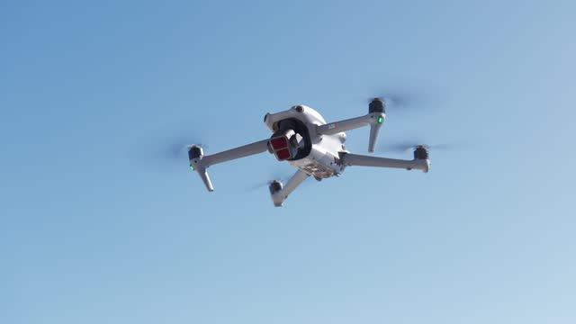 Modern white drone hovering with blue clear sky for copy space in background. Low angle view