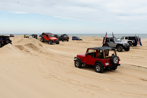 Virginia Beach, VA, USA - November 11, 2023
Red and black jeep climbing a sand dune obstacle at
the annual Jeep Fest held at Virginia Beach. Gathering of Jeep owners from across the country come to meet fellow jeep owners and practice new driving skills. A number of other jeeps in can bee seen in the background as they traverse the sand course that was made on the beach.