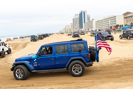 Virginia Beach, VA, USA - November 11, 2023
Blue jeep with a US Flag going around a sand course with other jeeps at the annual Jeep Fest held at Virginia Beach. Gathering of Jeep owners from across the country come to meet fellow jeep owners and practice new driving skills. A number of other jeeps in can bee seen in the background as they traverse the sand course that was made on the beach.