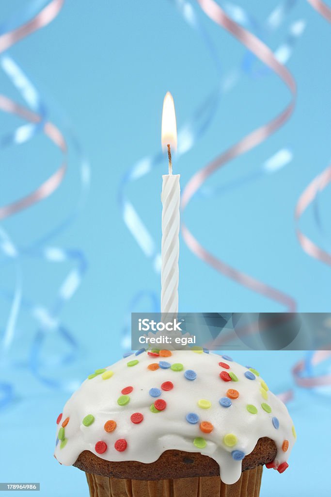 A birthday cupcake with white frosting and a lit candle birthday cupcake with white candle on blue background Anniversary Stock Photo