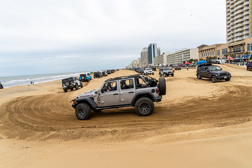 Virginia Beach, VA, USA - November 11, 2023\nA gray jeep going around a sand course with long lines of jeeps in the background at the annual Jeep Fest held at Virginia Beach, VA. Gathering of Jeep owners from across the country come to meet fellow jeep owners and practice new driving skills.