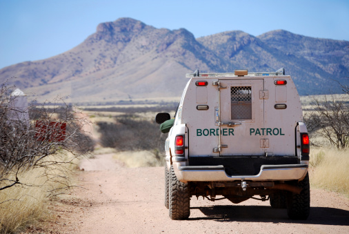 Back of a border patrol truck driving on a dirt road along the Mexican border in Arizona, with mountains in the background