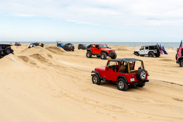 Virginia Beach, VA, USA - November 11, 2023\nRed jeep going over a sand obstacle at the annual Jeep Fest held at Virginia Beach, VA. Long lines of jeeps are seen going through the sand obstacle built on the beach. Gathering of Jeep owners from across the country come to meet fellow jeep owners and practice new driving skills.
