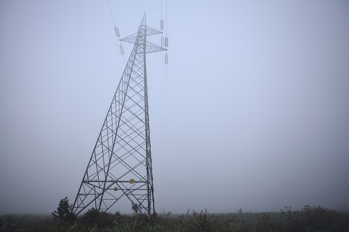 Electricity pylon in a field on a foggy day in the italian countryside