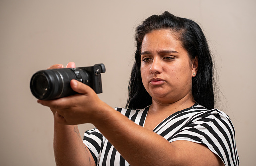 Young brunette woman holding a camera on pastel background.
