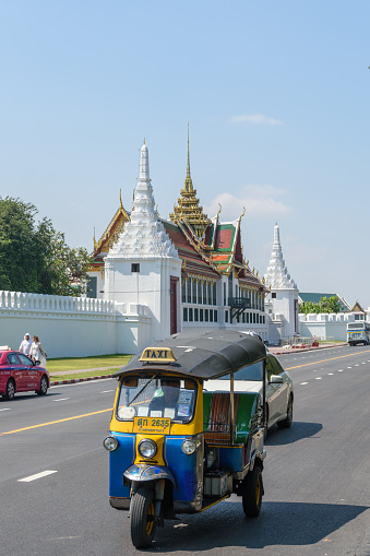 Samam Chai Rd, Bangkok, Thailand - March 19th 2018: Auto Rickshaw on Samam Chai Road. In the background is the Grand Palace and the Phra Thinang Suthaisawan Prasat hall in between the Deva Phithak and Sak Chaisit gates.
