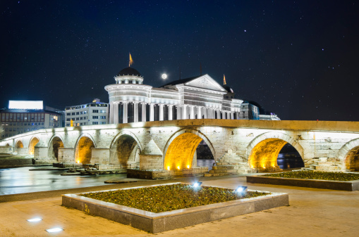 beautiful old stone bridge and baroc building on Vardar river bank in Skopje, Macedonia on star sky and moon