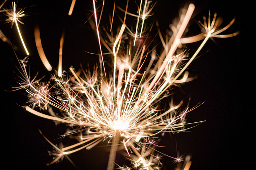 A poetic view of a sparkler sparking individual strands of light bursting into individual patterns resembling flowers and stars with the backdrop of a dark winters night sky