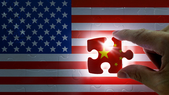 Hand holding piece of jigsaw puzzle with flag of China closing to the USA