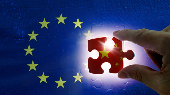 Hand holding piece of jigsaw puzzle with flag of China closing to the European Union