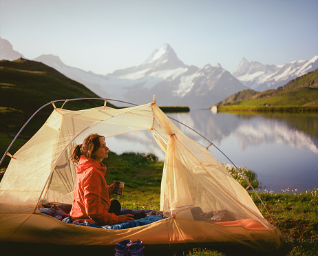 Cheerful woman drinking coffee in the tent near the idyllic lake in Swiss Alps