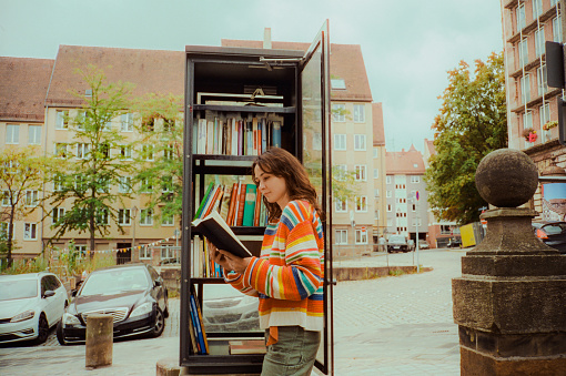 Woman reading book from book crossing shelf in the city. Shot on camera film