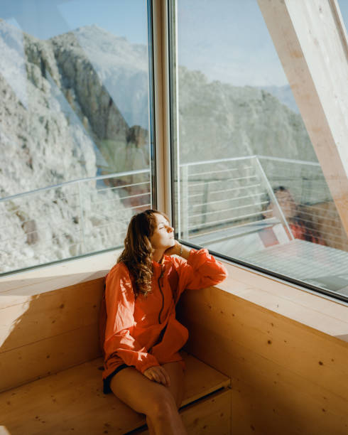 woman looking through the window in alpine shelter at the view of dolomites - home interior cabin shack european alps imagens e fotografias de stock