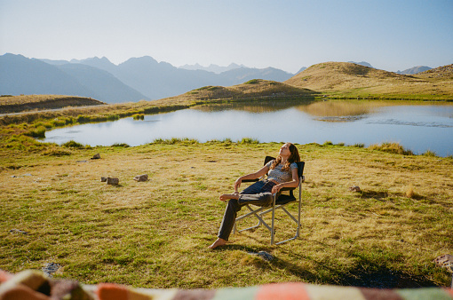 Relaxed woman sitting on folding chair near the lake during camper van trip to Alps