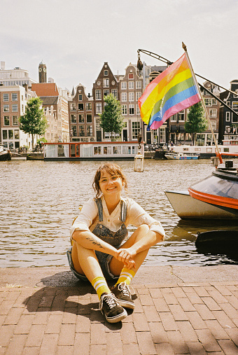 Portrait of  woman sitting on the background of LGBTQ+ flag on the boat in Amsterdam. Shot on camera film