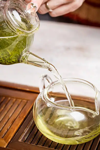 Teapot pouring green tea into a cup