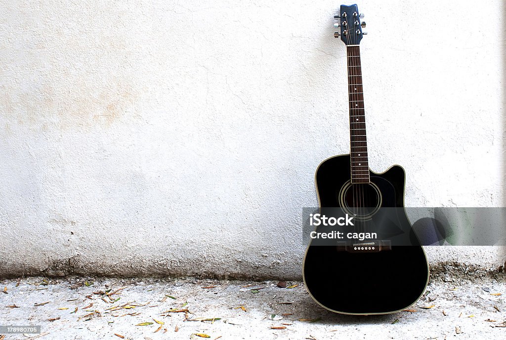 A black singular guitar against a wall Guitar, standing next to a white wall. Acoustic Guitar Stock Photo