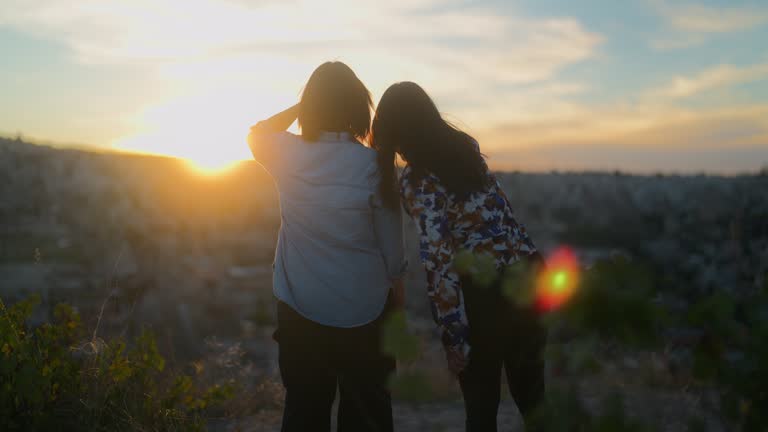 Two female tourist friends watching the sunset from top of hill in Cappadocia in Türkiye Turkey