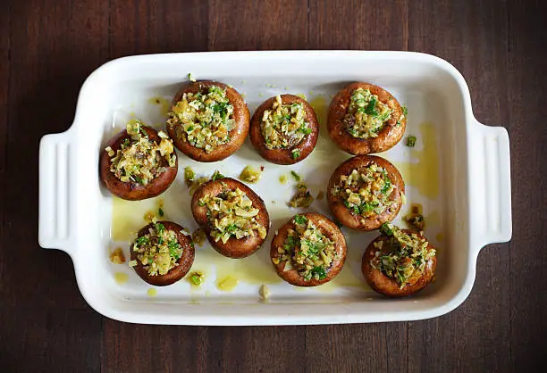 Button, portobello mushrooms stuffed with cheese and herbs with olive oil in a baking dish