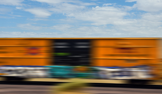 A brightly colored box car races through a desert scene on a cloudy day