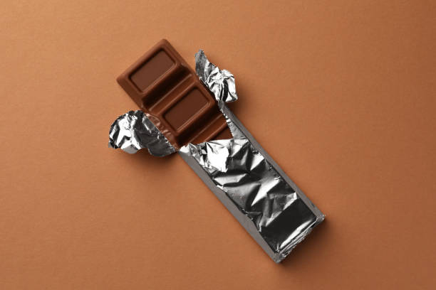 istock Delicious chocolate bar wrapped in foil on light brown background, top view 1789873632