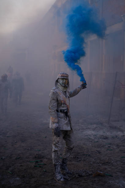 homem vestido de soldado olhando para câmera com bomba de fumaça azul na mão em tradicional batalha de farinha em ibi, espanha - firework display traditional festival bomb explosive - fotografias e filmes do acervo