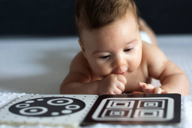 A baby looks at a black and white contrast educational book. Intellectual development of newborns. Developing cards for children.