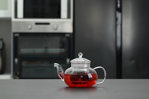 Glass teapot with delicious tea on grey table in kitchen