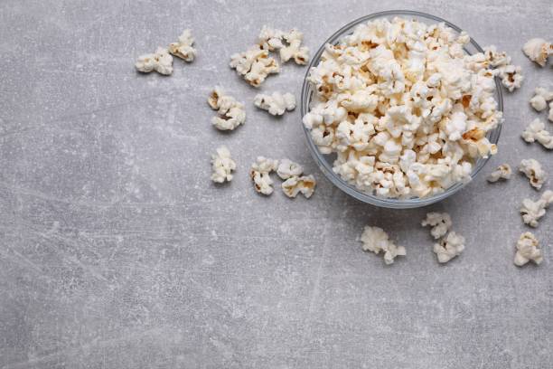 Bowl of tasty popcorn on grey table, flat lay. Space for text
