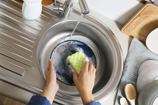 Woman washing plate in kitchen sink, above view