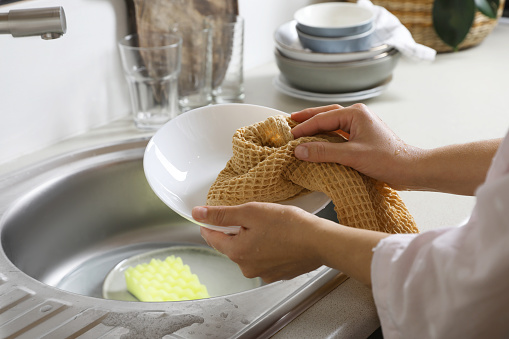 Woman wiping plate with towel in kitchen , closeup