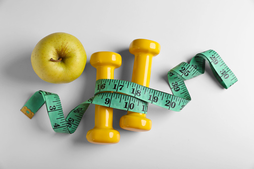 Measuring tape, dumbbells and apple on white background, flat lay. Weight control concept