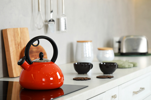 Red kettle with whistle on cooktop in kitchen. Space for text