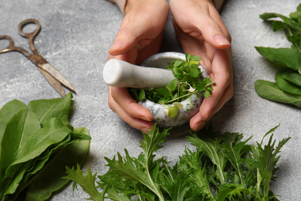 istock Woman grinding fresh green herbs in mortar at light grey table, closeup 1789914464
