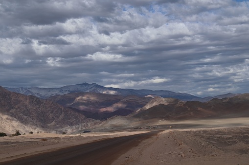 A desolate dirt road stretches across a barren desert landscape, leading to a distant vanishing point