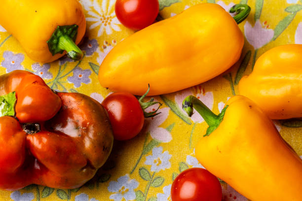 Ripe red tomatoes and yellow peppers on a table.