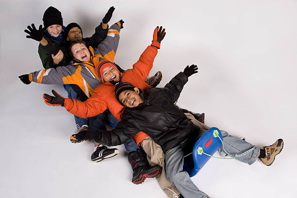 Let's Sled Isolated image of five young boys of diverse cultures all bundled up and sledding recklessly down the snowcovered hill. kids winter coat stock pictures, royalty-free photos & images