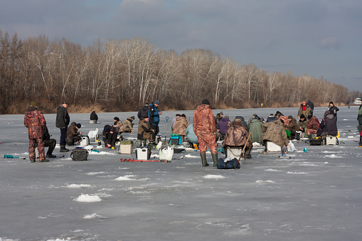 Dnipro, Ukraine - February 09, 2022: Large group of fishermen on winter ice fishing. Many people are fishing on the ice-covered river. Sunny day. Winter landscape.