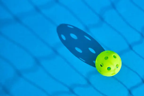 Photo of green pickleball ball on blue surface with the shadow of a net in front