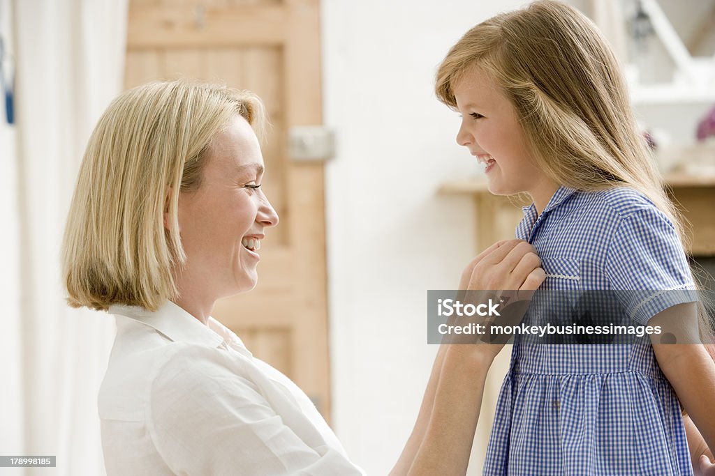 Woman in front hallway fixing young girl's dress Woman in front hallway fixing young girl's dress kneeling down looking at each other smiling Getting Dressed Stock Photo
