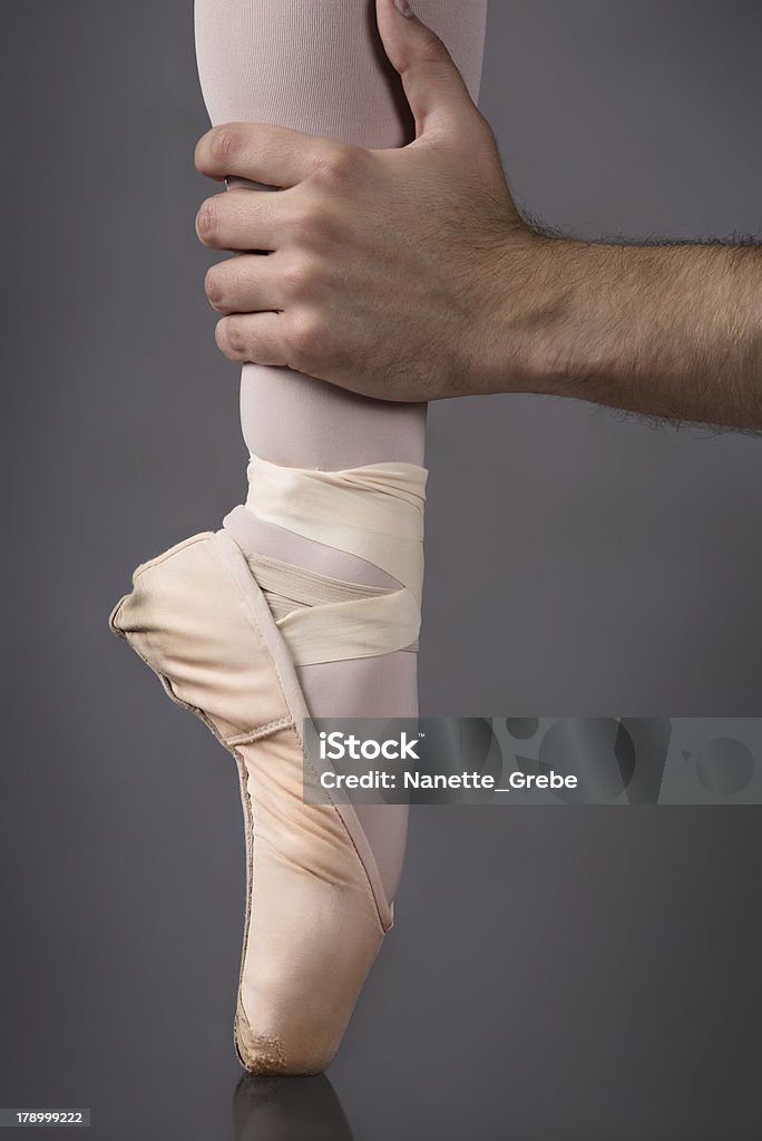 Female ballet dancer Male hand grasping the ankle of a female ballet dancer's foot in a pink pointe shoe. Adult Stock Photo