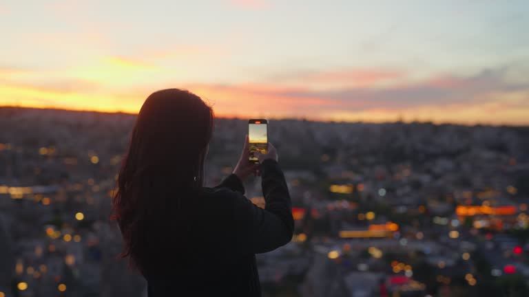 Multiracial female tourist using her mobile smart phone to take photos of sunset from top of hill in Cappadocia Türkiye Turkey