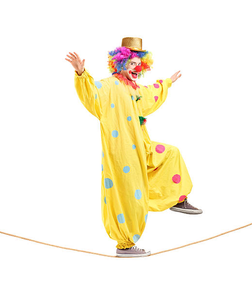 Full length portrait of a happy male clown walking on a rope isolated on white background