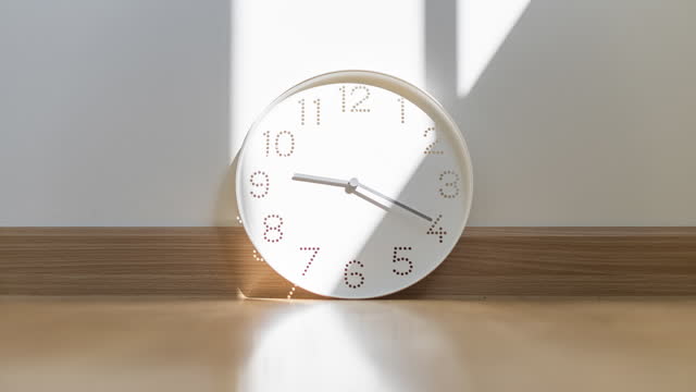 Bright sunlight and window frame's shadow moving pass a clock on wooden floor which is ticking from 8.30 to 10.30 a.m. during sunrise in a living room.